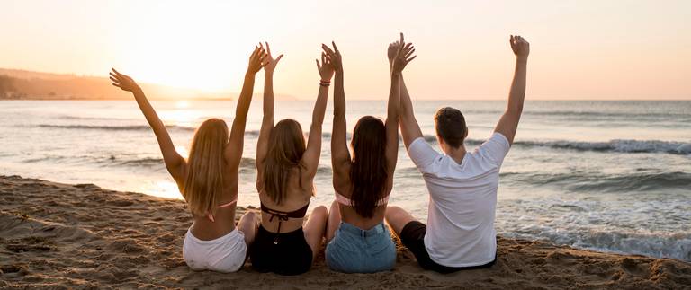 Gruppe von Freunden, die am Meer sitzen und die Arme in die Luft strecken Gruppe von Freunden, die am Meer sitzen und die Arme in die Luft strecken